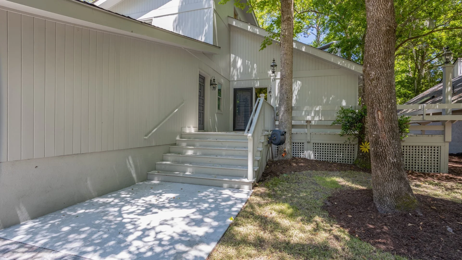 Exterior view of a light-painted house with stairs leading to a front door, surrounded by trees and greenery.