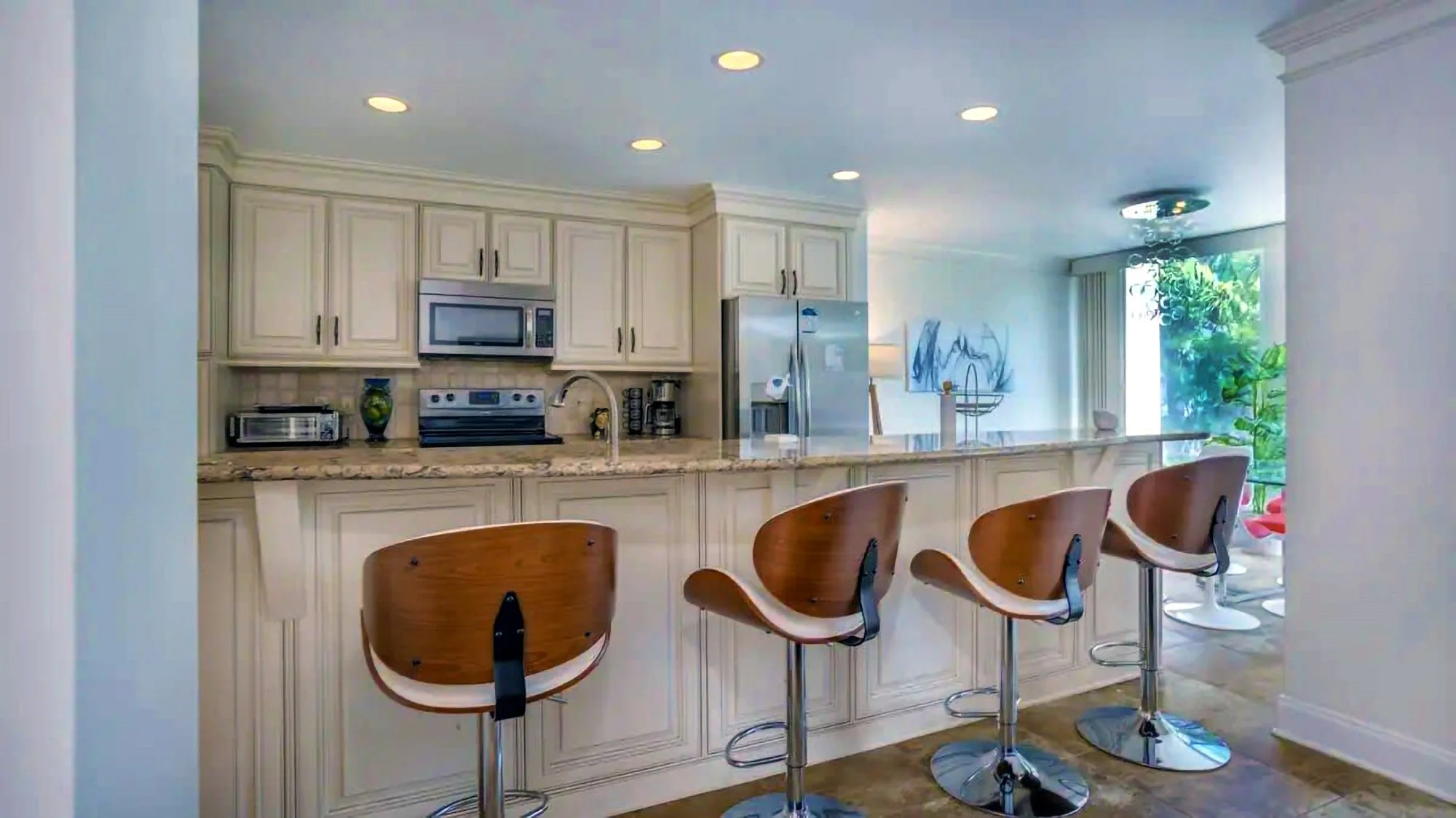 Modern kitchen with bar stools, white cabinets, stainless steel appliances, and granite countertops.