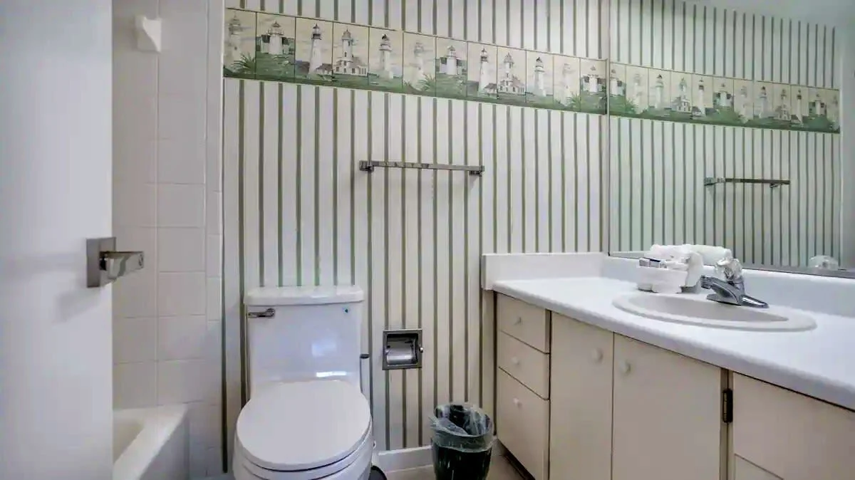 Bathroom with striped wallpaper, toilet, countertop with sink, faucet, rolled towels, towel rack, and nautical border design.