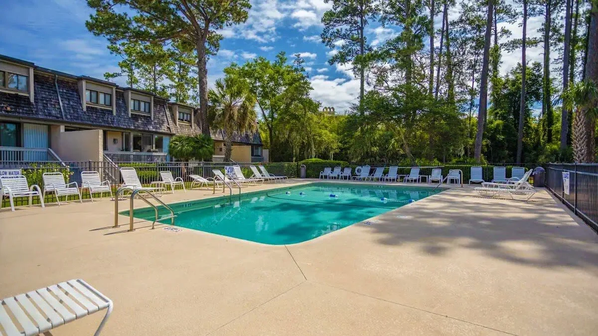 Outdoor swimming pool with lounge chairs and trees in the background.