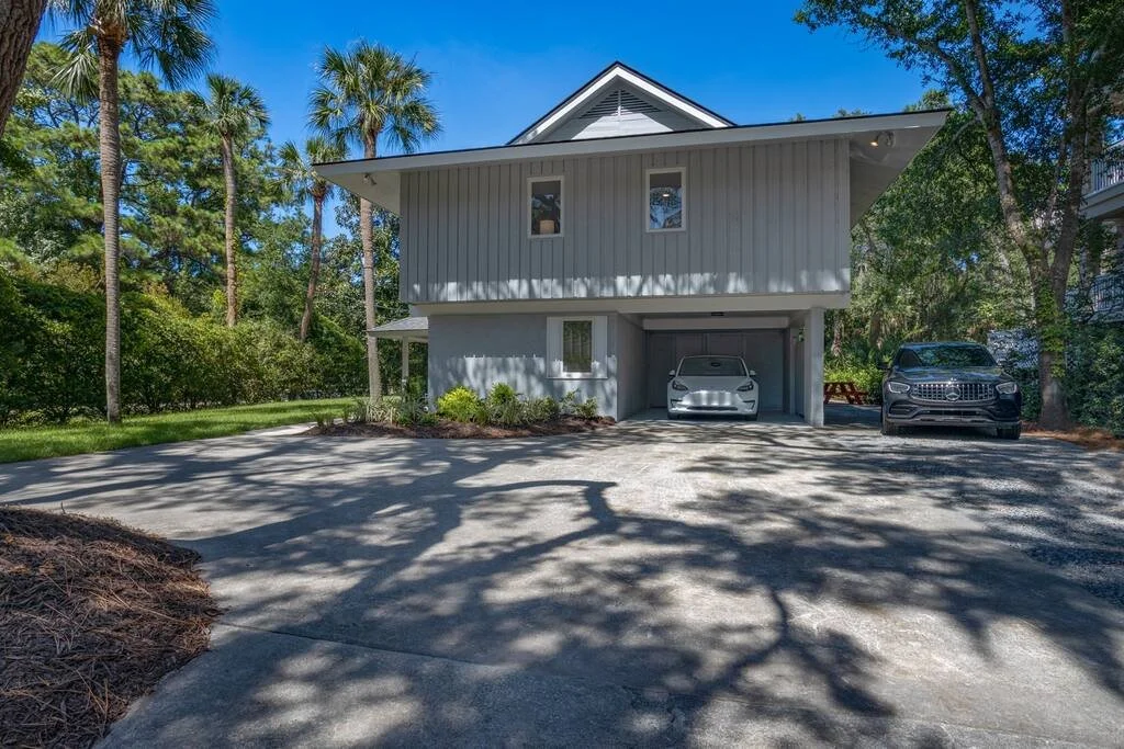 Modern house with palm trees, driveway, parked white and black cars, sunny day