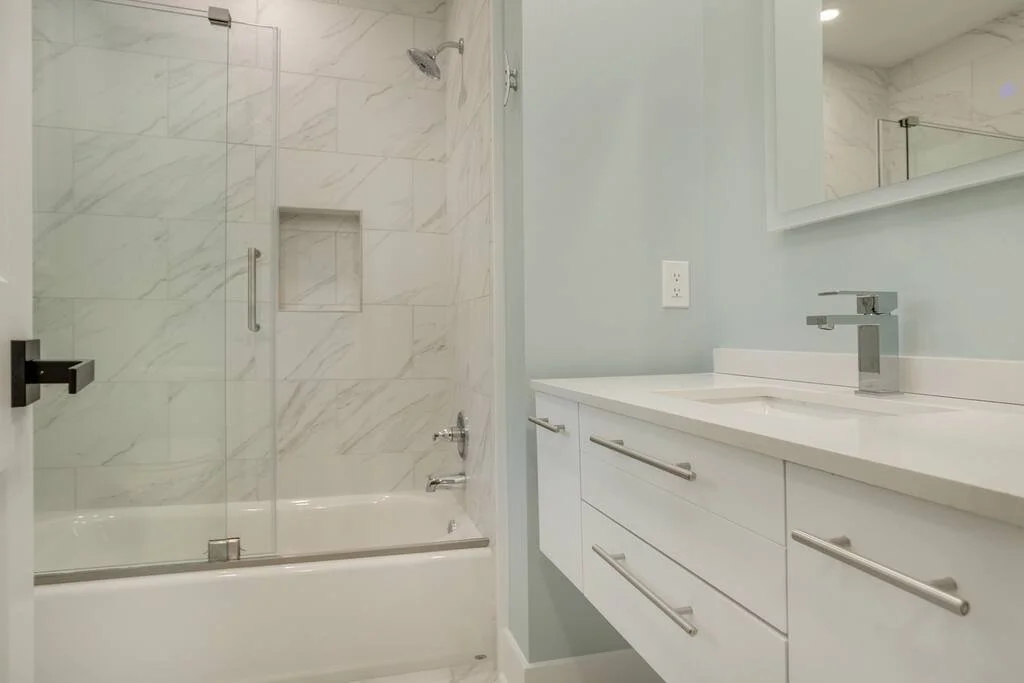 Modern bathroom with a glass shower enclosure, marble tiles, white vanity with drawers, and a single faucet.