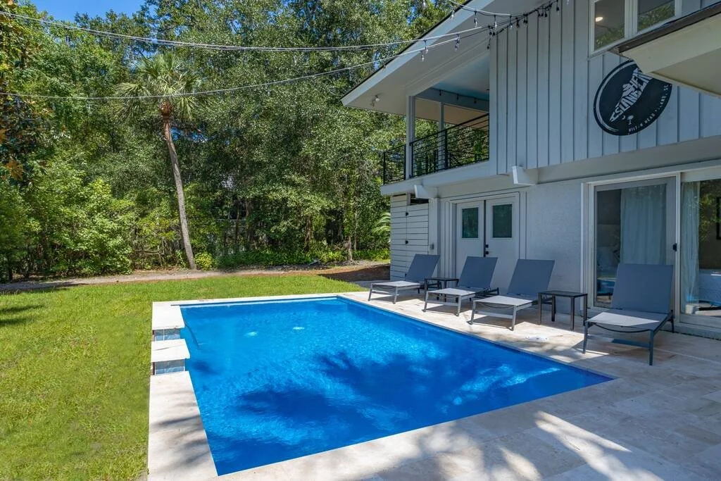 House with a backyard pool, lounge chairs, and forested surroundings.