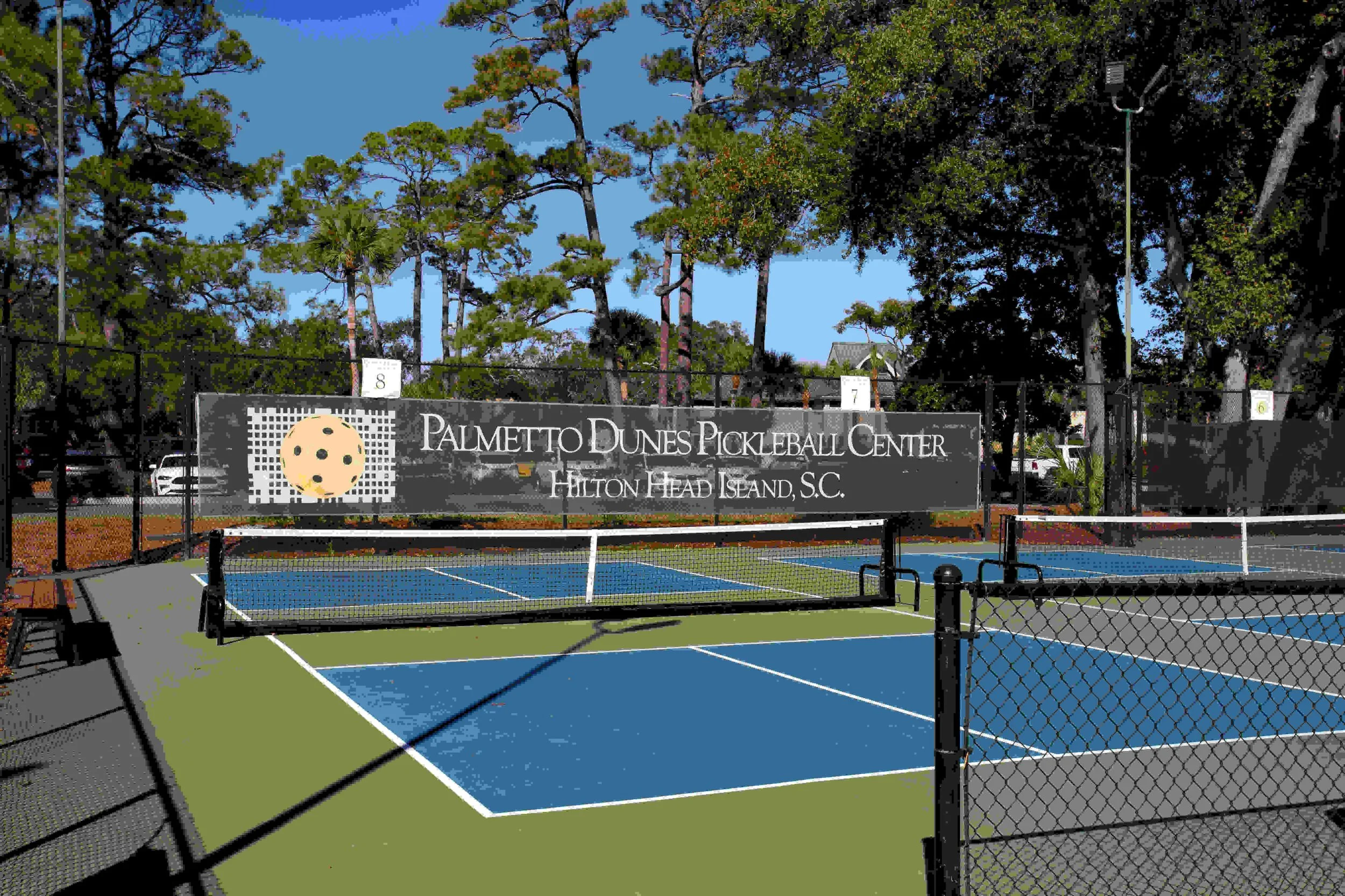 Pickleball courts at Palmetto Dunes Pickleball Center, Hilton Head Island, South Carolina, surrounded by trees and a sign displaying the center's name.