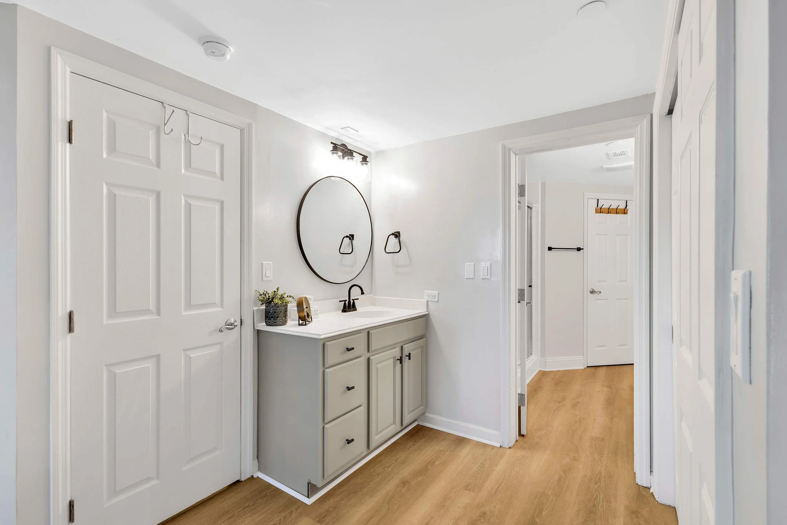 Modern bathroom with round mirror, white vanity, and wood flooring