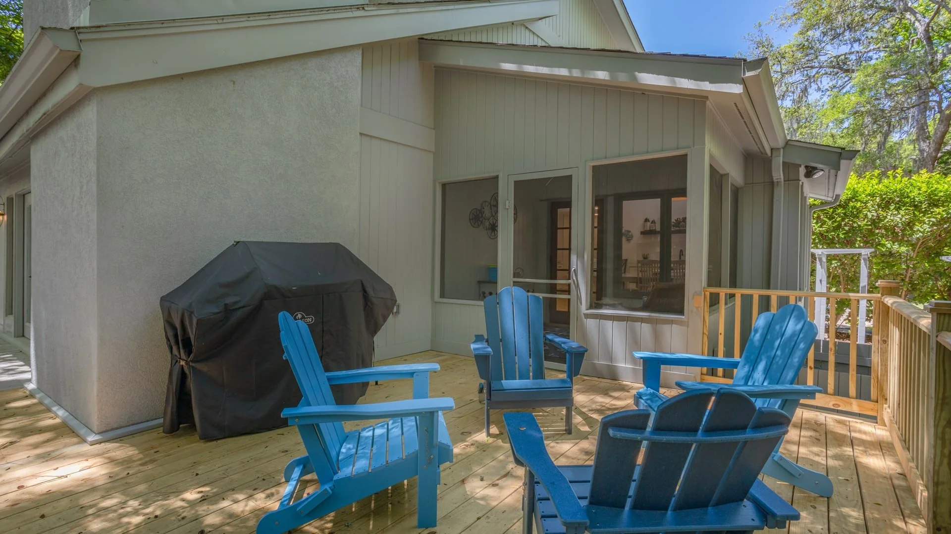 Outdoor patio with blue Adirondack chairs, a covered grill, and wooden deck
