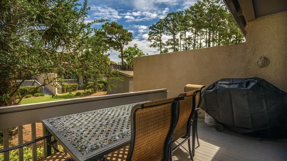 Outdoor patio with table and chairs, barbecue grill, trees, and a view of neighboring houses.