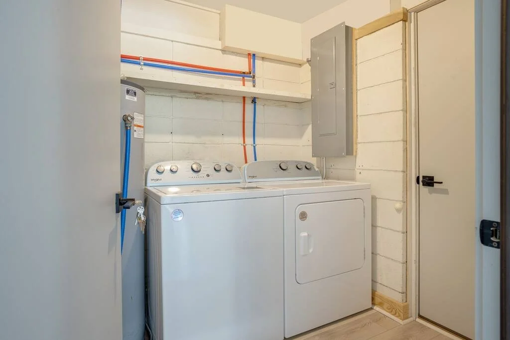 Laundry room with a washer and dryer, pipes on the wall, and a closed door.