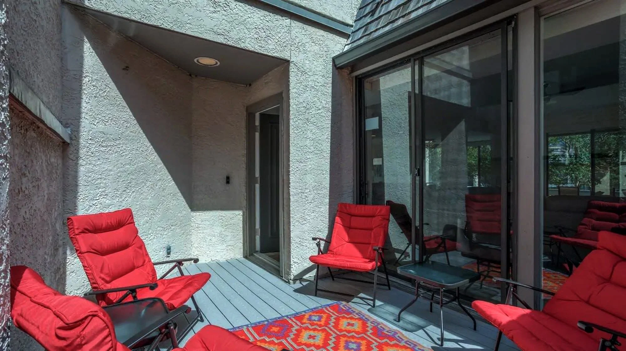 Outdoor patio with red cushioned chairs and a colorful geometric rug.