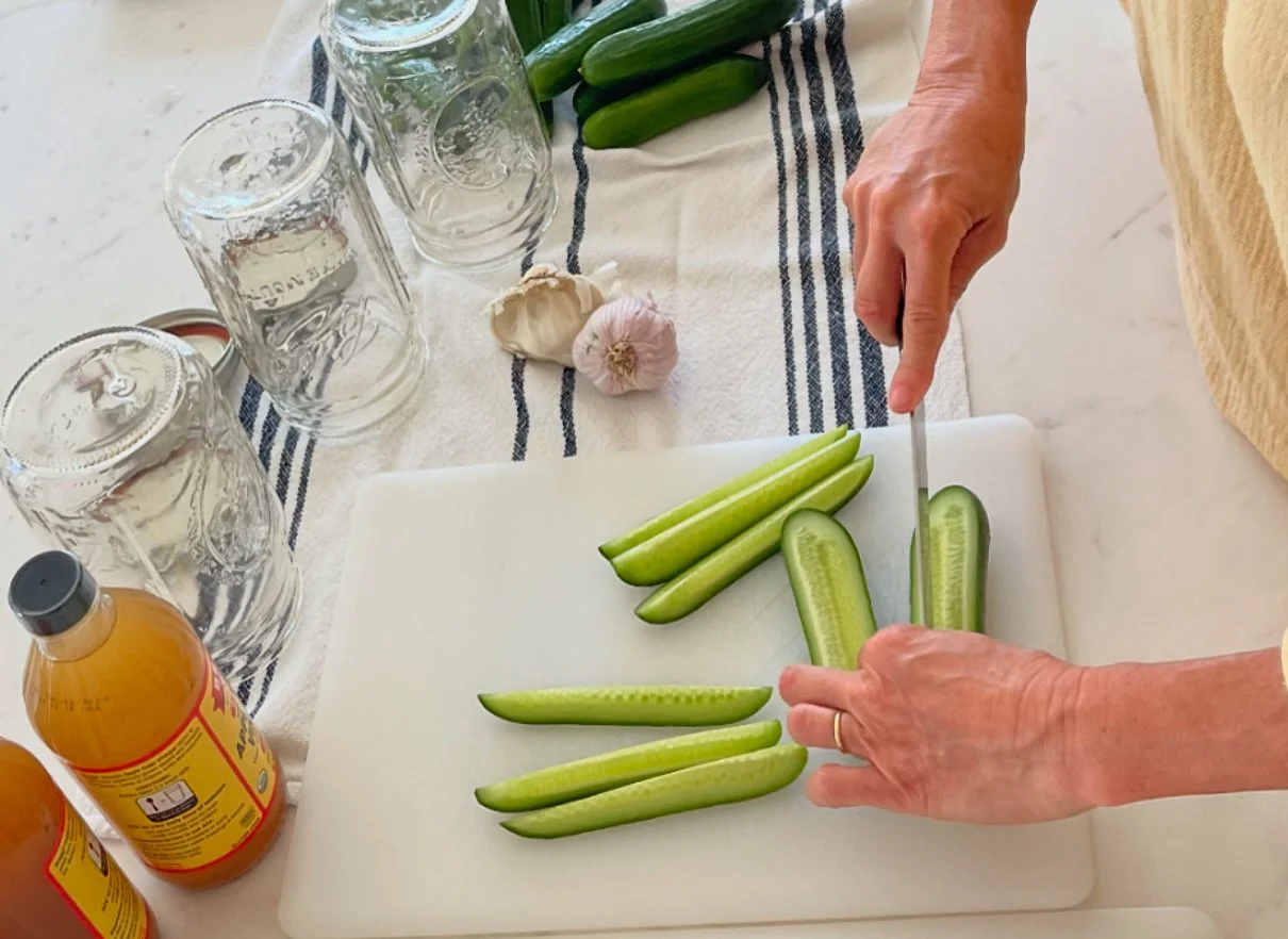 Slicing mini cucumbers on a cutting board with mason jars and garlic.