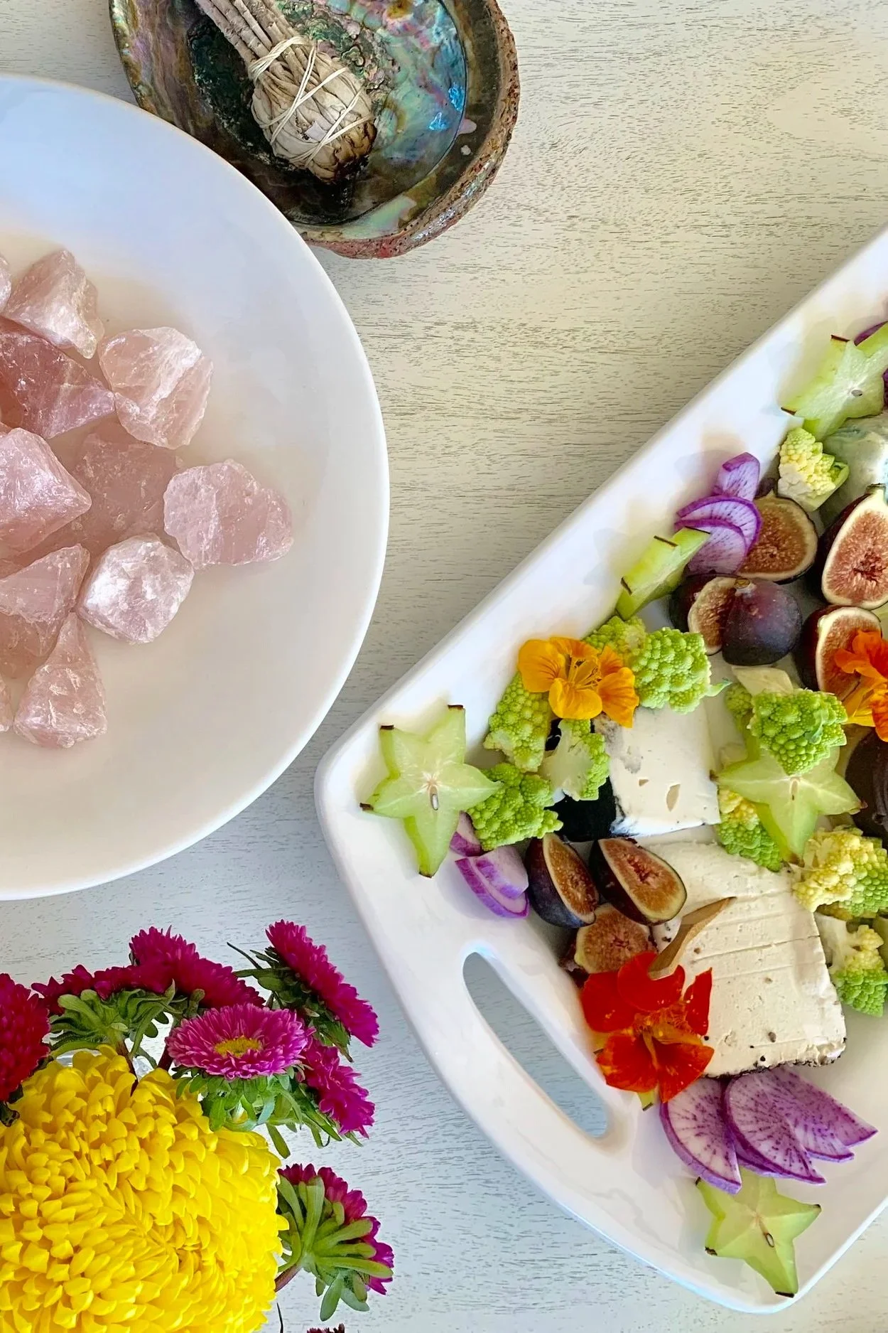 A vegan cheese plate and charcuterie board with edible flowers, purple daikon, romanesco, star fruit, and figs