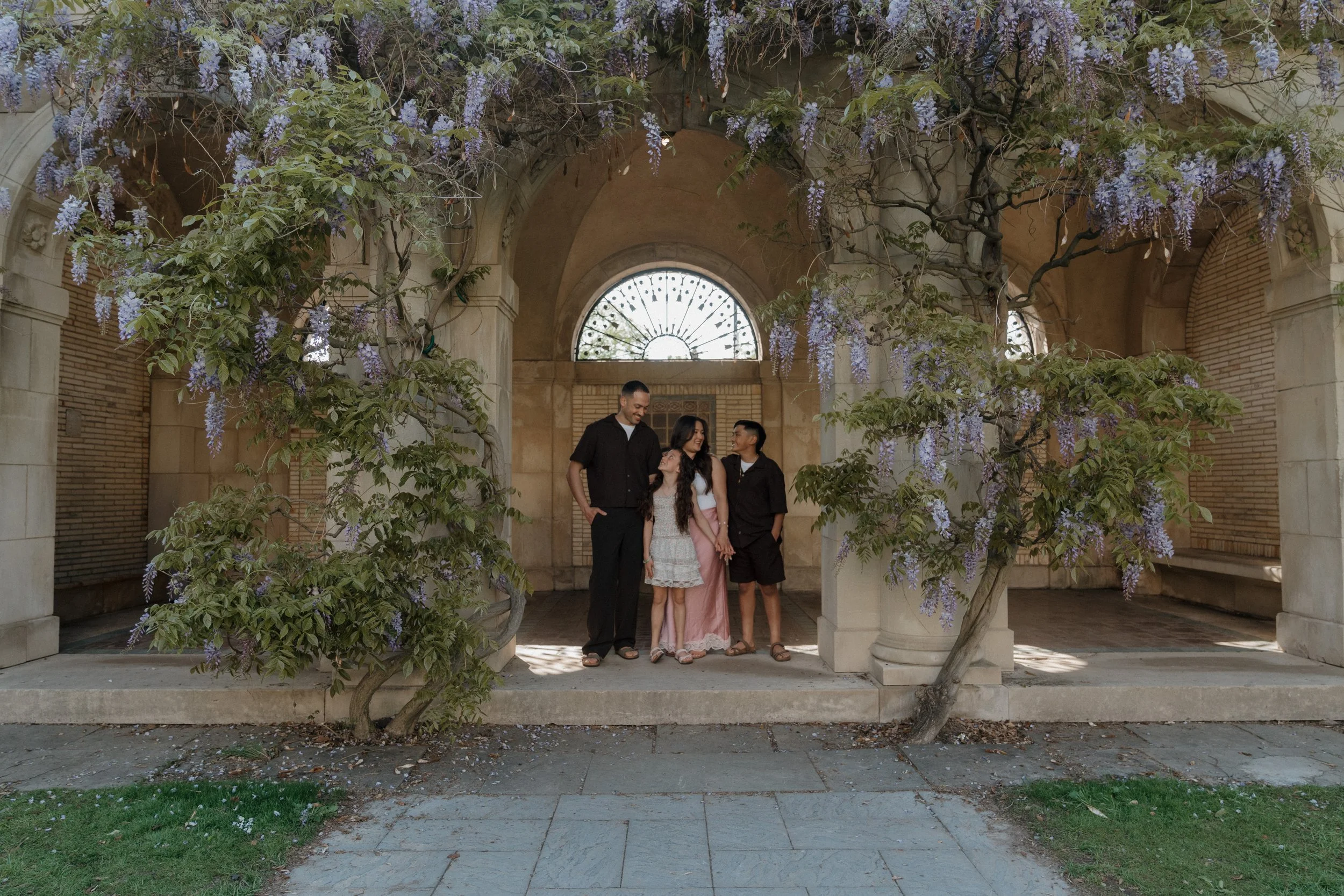 Family standing together beneath blooming wisteria during an outdoor family photography session in Sarasota, Florida.