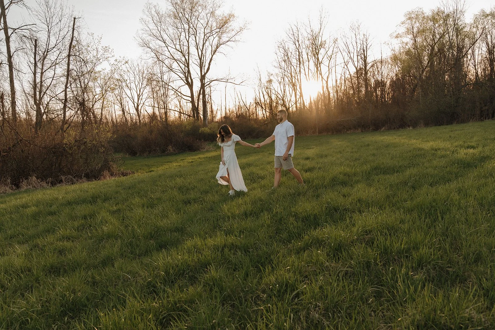 Couple walking through a sunlit field during a romantic sunset engagement session in Sarasota, Florida.