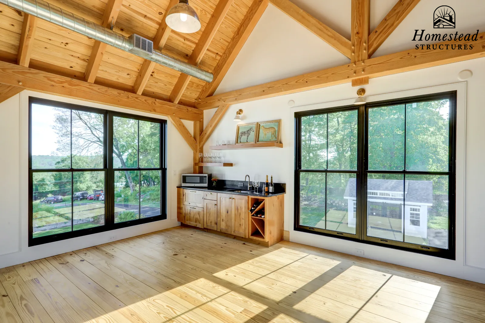 Interior of a modern room with large windows, wooden ceiling and floors, a kitchenette with a microwave, and wall art with animals.