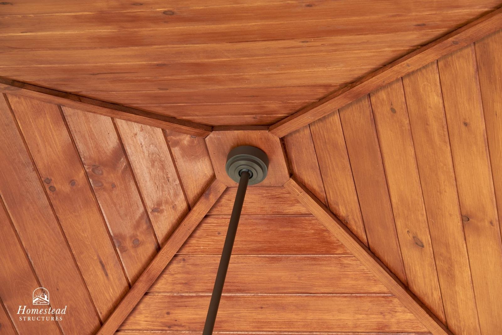 Upward view of a wooden gazebo roof with a central black support pole