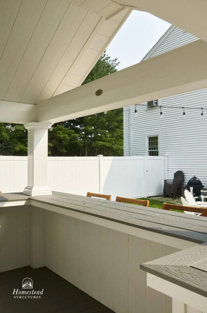 View from a porch showing outdoor chairs, a fence, and string lights in a backyard.