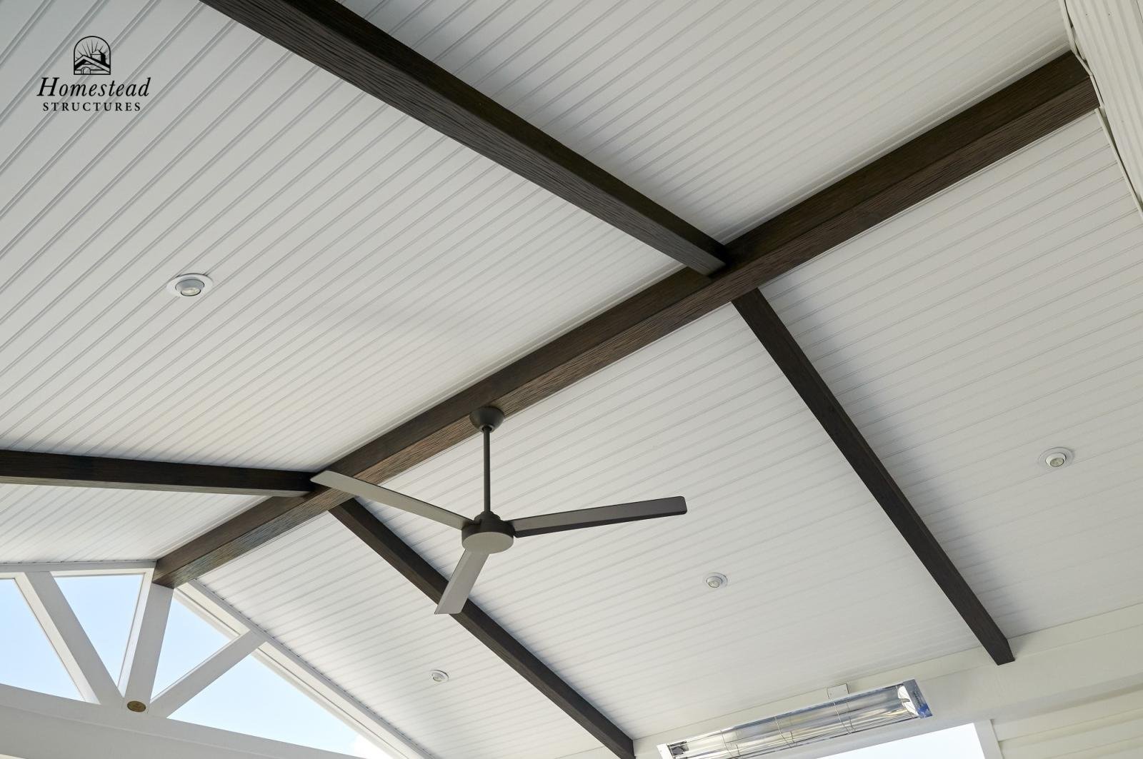 Ceiling of a porch with white beadboard ceiling, dark wood beams, a ceiling fan, and several recessed lights.
