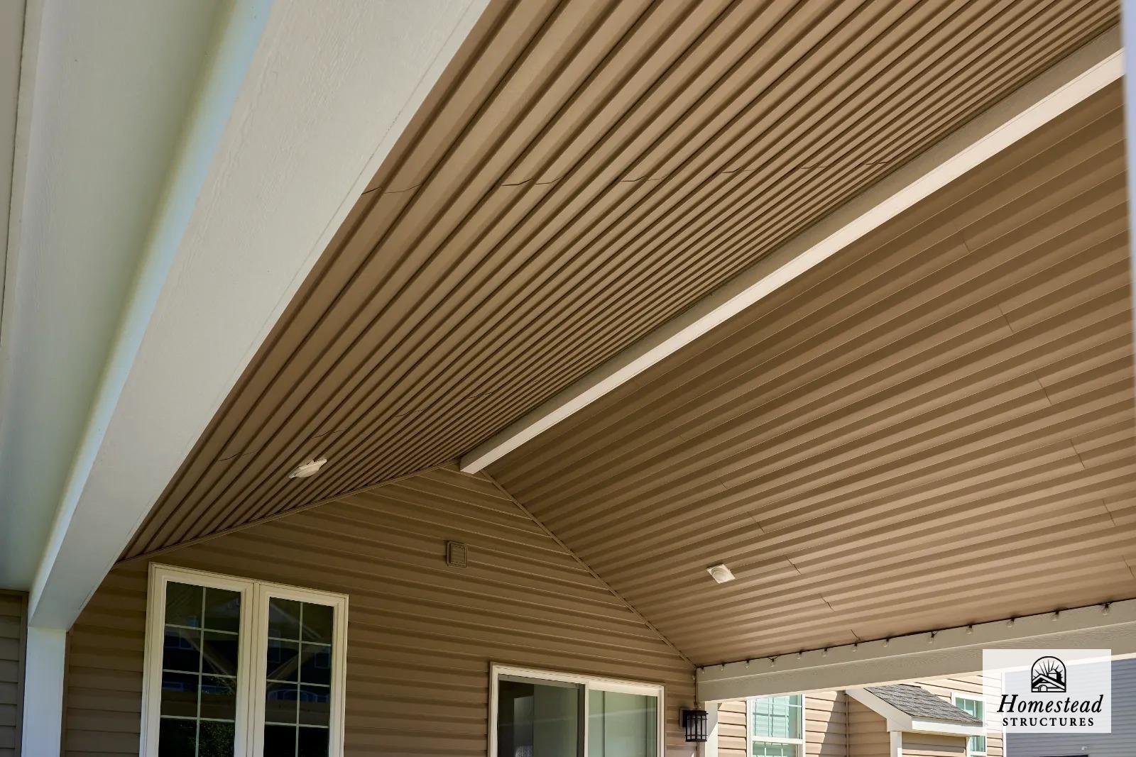 Close-up of an outdoor covered porch with a sloped beige metal roof, beige siding, white trim around the window, and a black lantern-style light fixture.