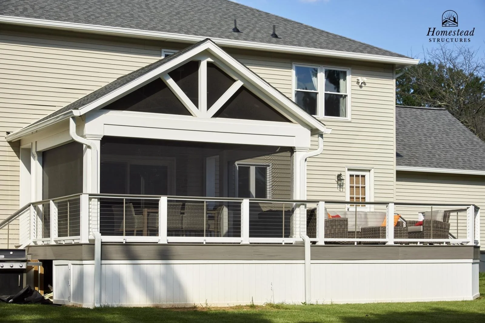 A house with a screened-in porch and outdoor furniture, including chairs and a table, on a wooden deck with white railings.
