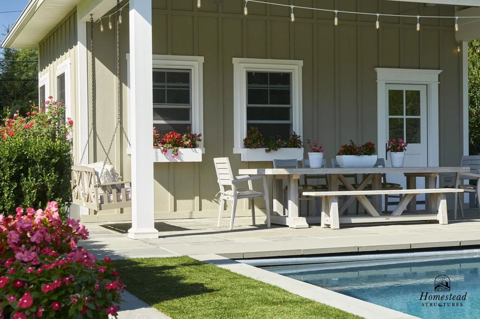 A backyard porch with outdoor furniture, potted flowers, a swing, and a swimming pool.