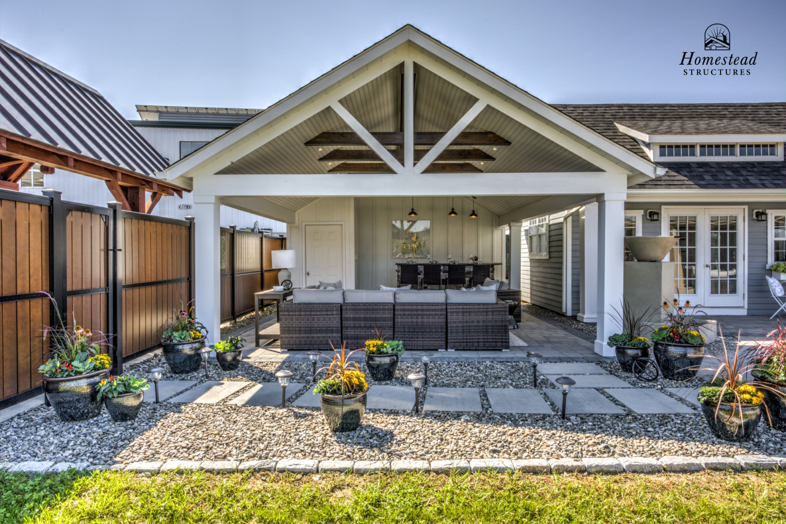 Covered outdoor patio with wicker furniture, potted plants, pathway, and surrounding house
