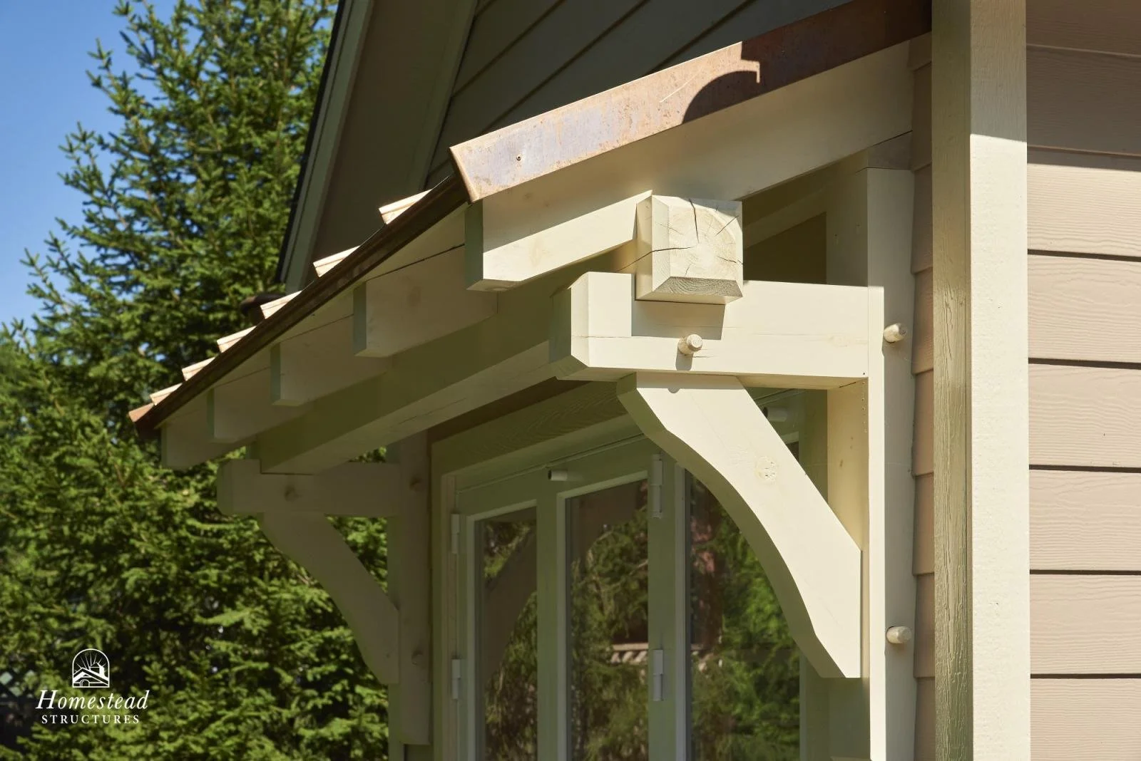 Close-up view of a corner of a house with beige siding, new wooden trim, and decorative brackets under the eaves, with a new window and trees in the background.