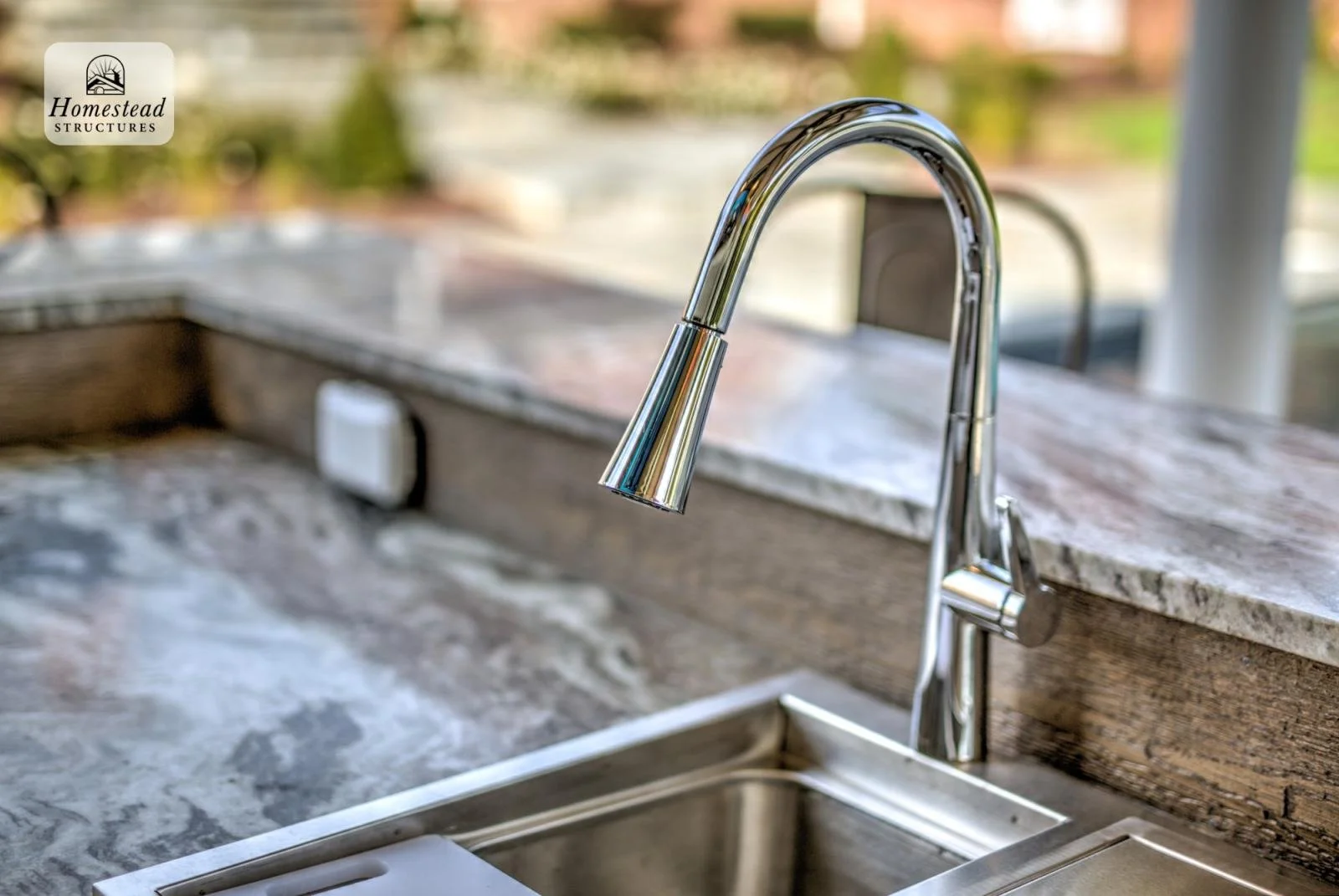 Close-up of a modern chrome kitchen faucet over a stainless steel sink with a granite countertop.