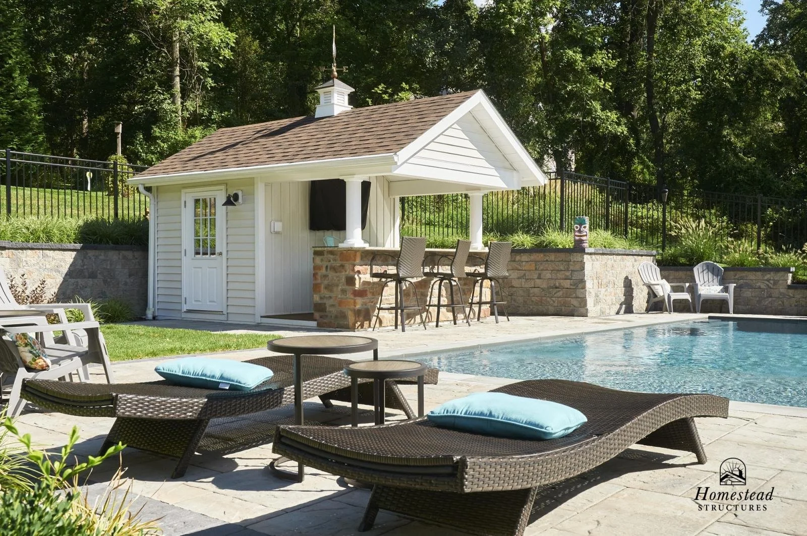 Backyard with a swimming pool, patio furniture, a small white pool house, and lush greenery in the background.