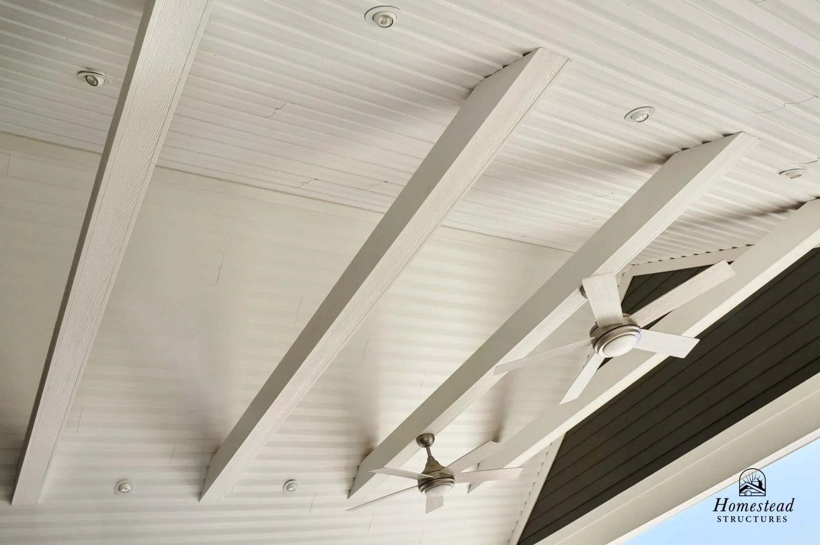 Ceiling with white wooden beams and two ceiling fans, with small recessed lights.
