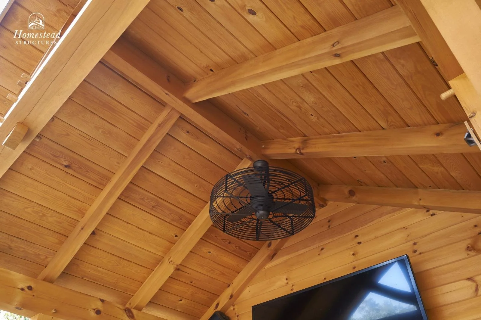 Wood-paneled ceiling with black ceiling fan and a flat-screen TV mounted on the wall, in a rustic home interior.