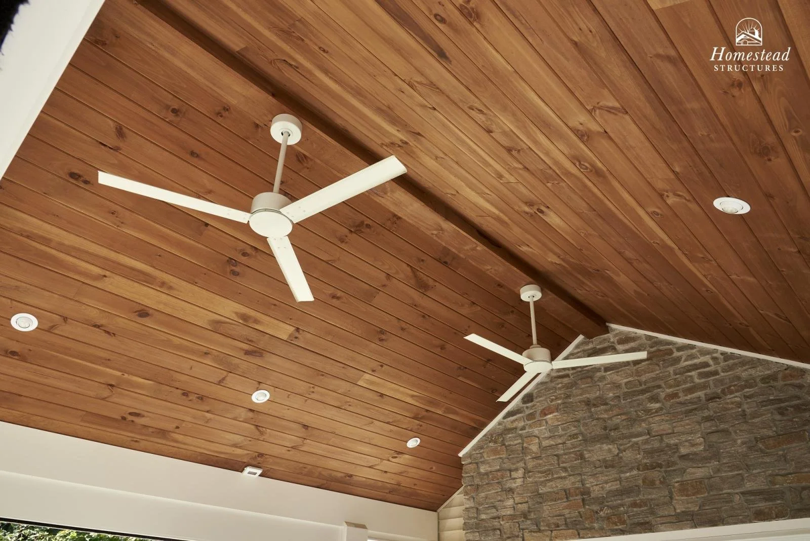 Wood-paneled ceiling with two white ceiling fans, recessed lights, and a section of brick wall visible.