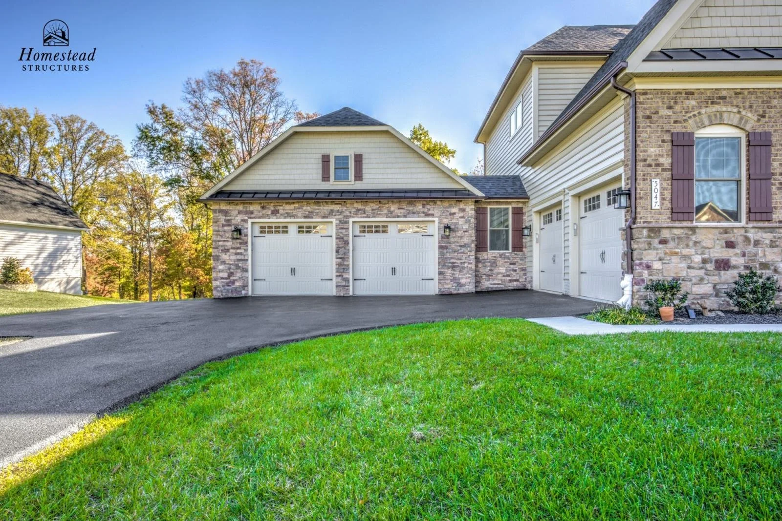 Modern house with a stone and siding exterior, two garage doors, and a well-maintained lawn in a suburban neighborhood.