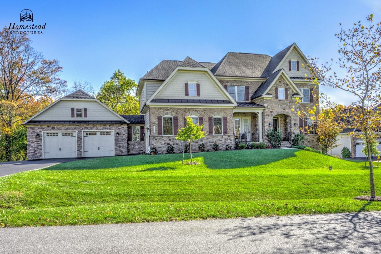 Large, two-story house with brick and siding exterior, multiple gabled roofs, and attached two-car garage, surrounded by green lawn and trees, under clear blue sky.