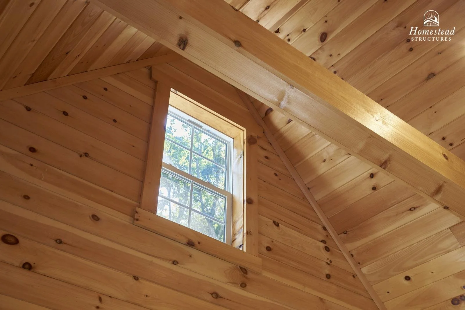 Interior view of a wooden ceiling with a rectangular window showing trees outside.