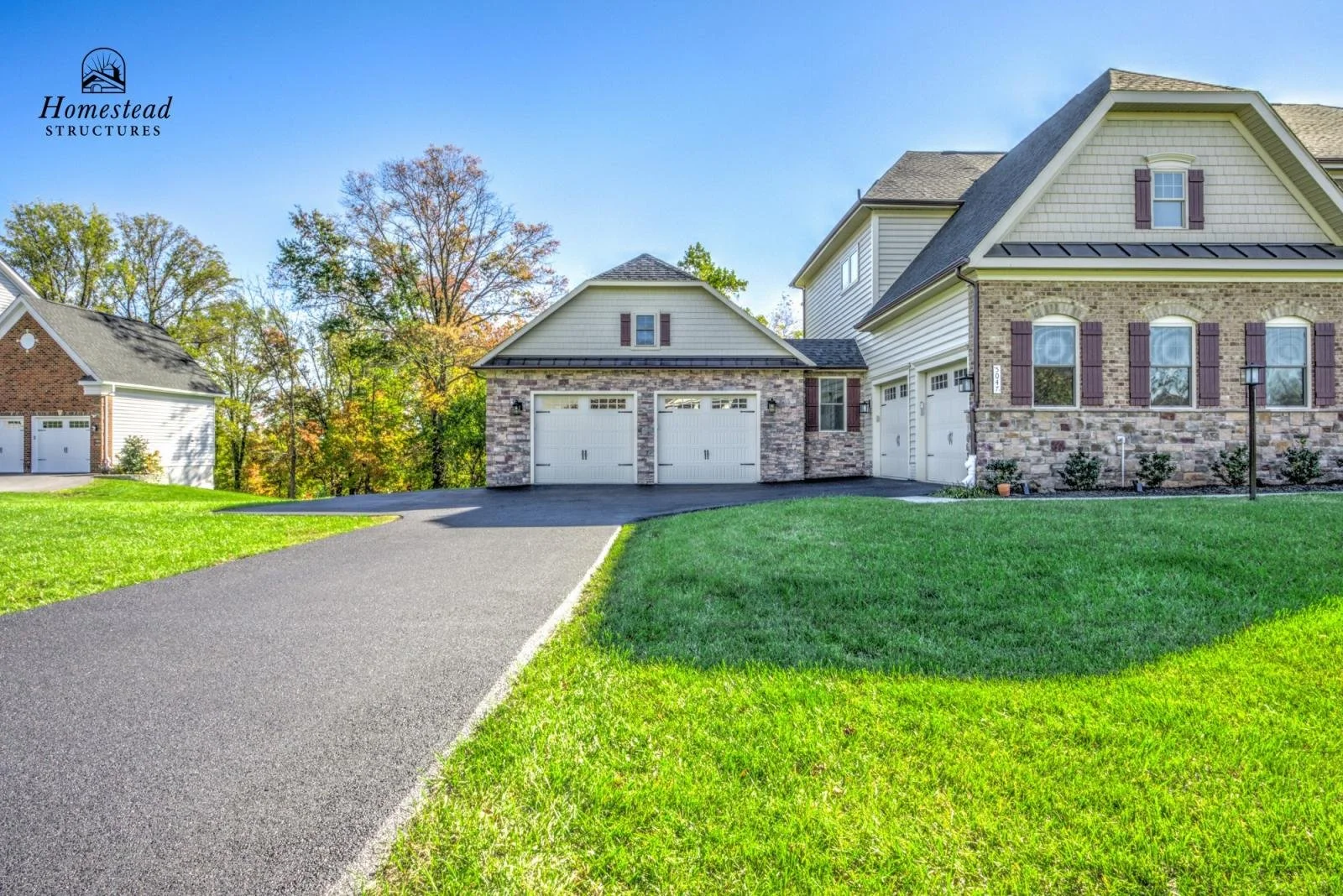 A newly built house with a paved driveway, a double garage with white doors, brick and siding exterior, green lawn, and trees in the background.