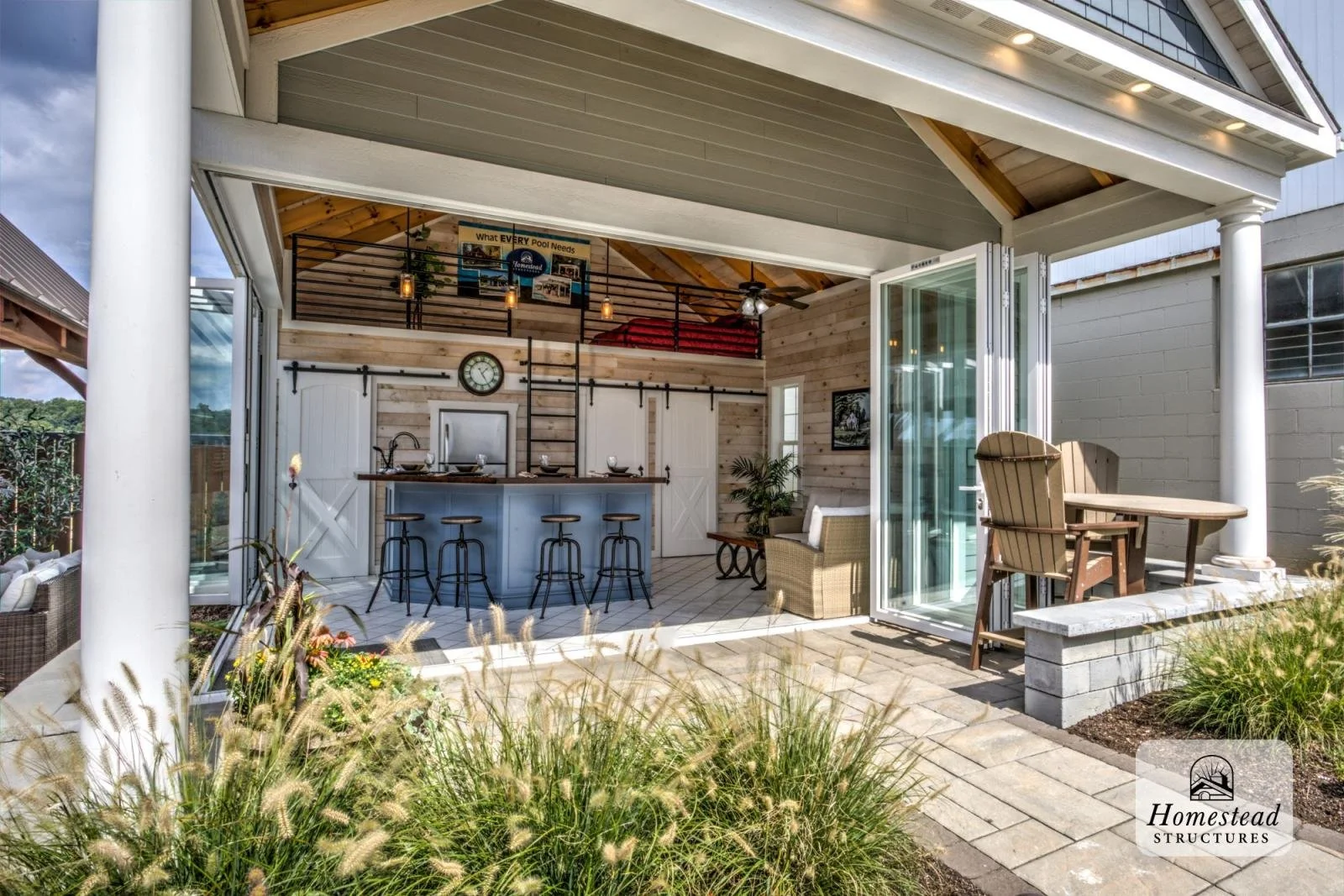 Outdoor living area featuring a covered patio with sliding glass doors, a bar with three stools, a seating area with a sofa and coffee table, a table with chairs, and decorative plants.