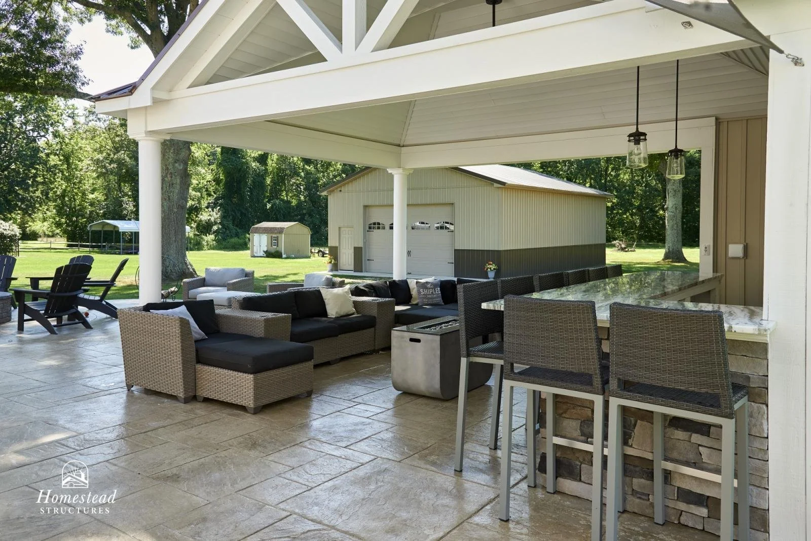 Covered outdoor patio with seating area, bar counter, and a view of a grassy backyard with trees and a shed.