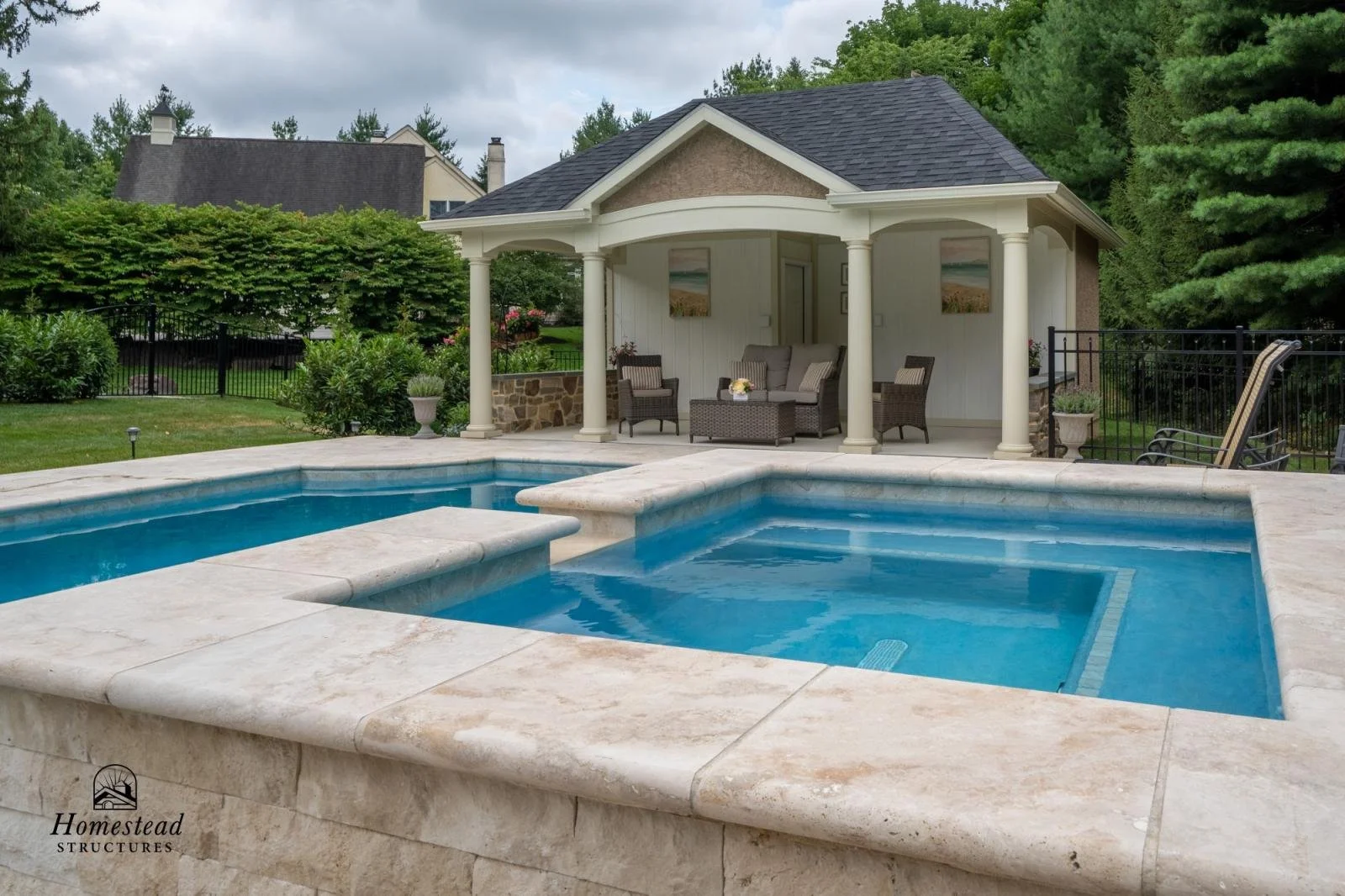 A backyard featuring a swimming pool with a hot tub, a covered patio with seating, surrounded by greenery and trees.