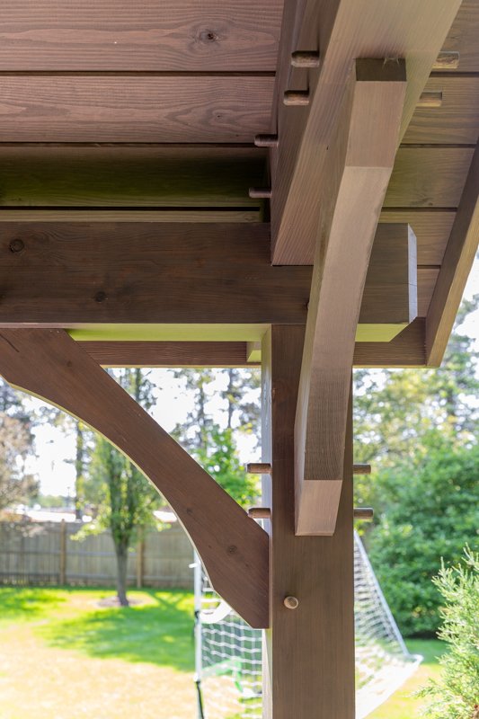 Close-up of a wooden backyard treehouse support beam and platform with a backyard and trees in the background.