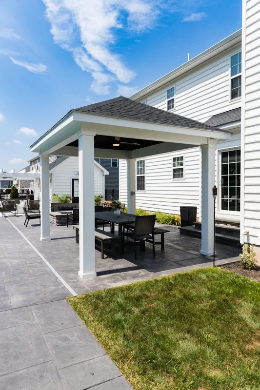 Residential backyard with a white patio gazebo, outdoor furniture, and a black paved patio on a sunny day.