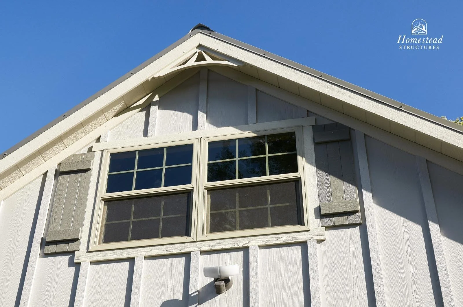 Close-up of a white house with textured siding, large window with grid panes, on a sunny day with clear blue sky, and a small security camera mounted below the window.