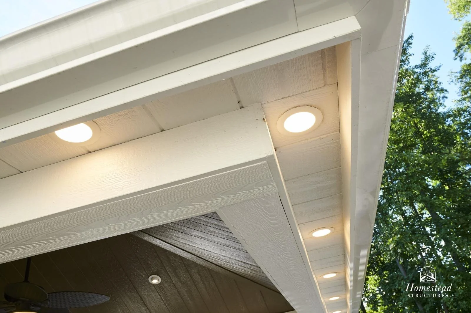 Close-up of white house eaves with built-in round lights, trees in background.