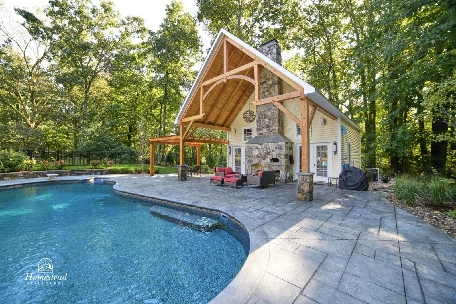 Backyard with swimming pool, patio, outdoor fireplace, and house with large wooden roof overhang, surrounded by trees.