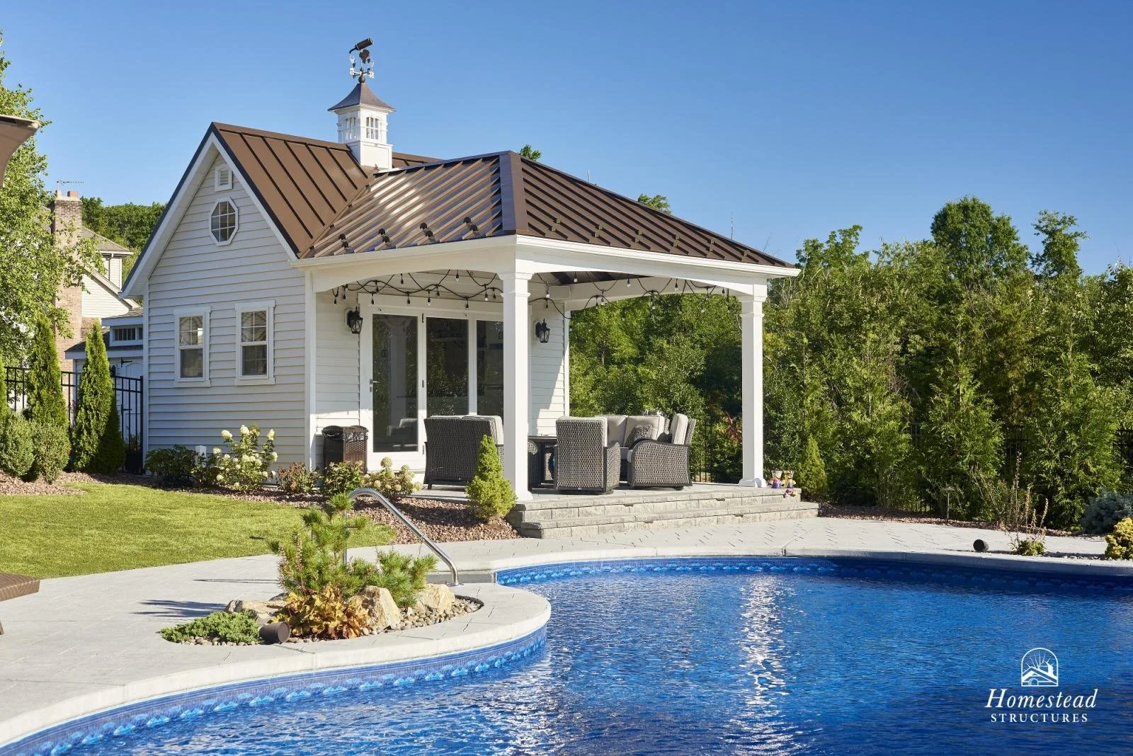A backyard with a pool and a white house with a covered patio, outdoor seating, and landscaping.