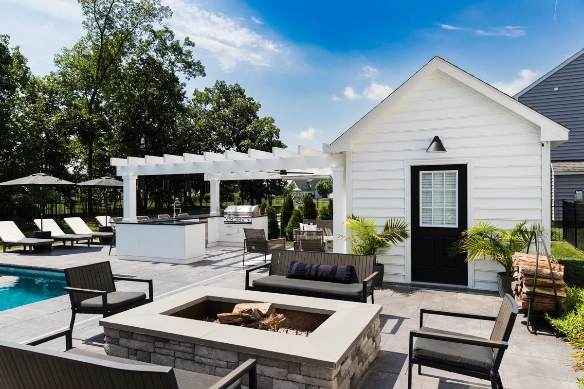 Backyard with pool, fire pit, outdoor seating, swim-up bar, and a small white building with a black door.