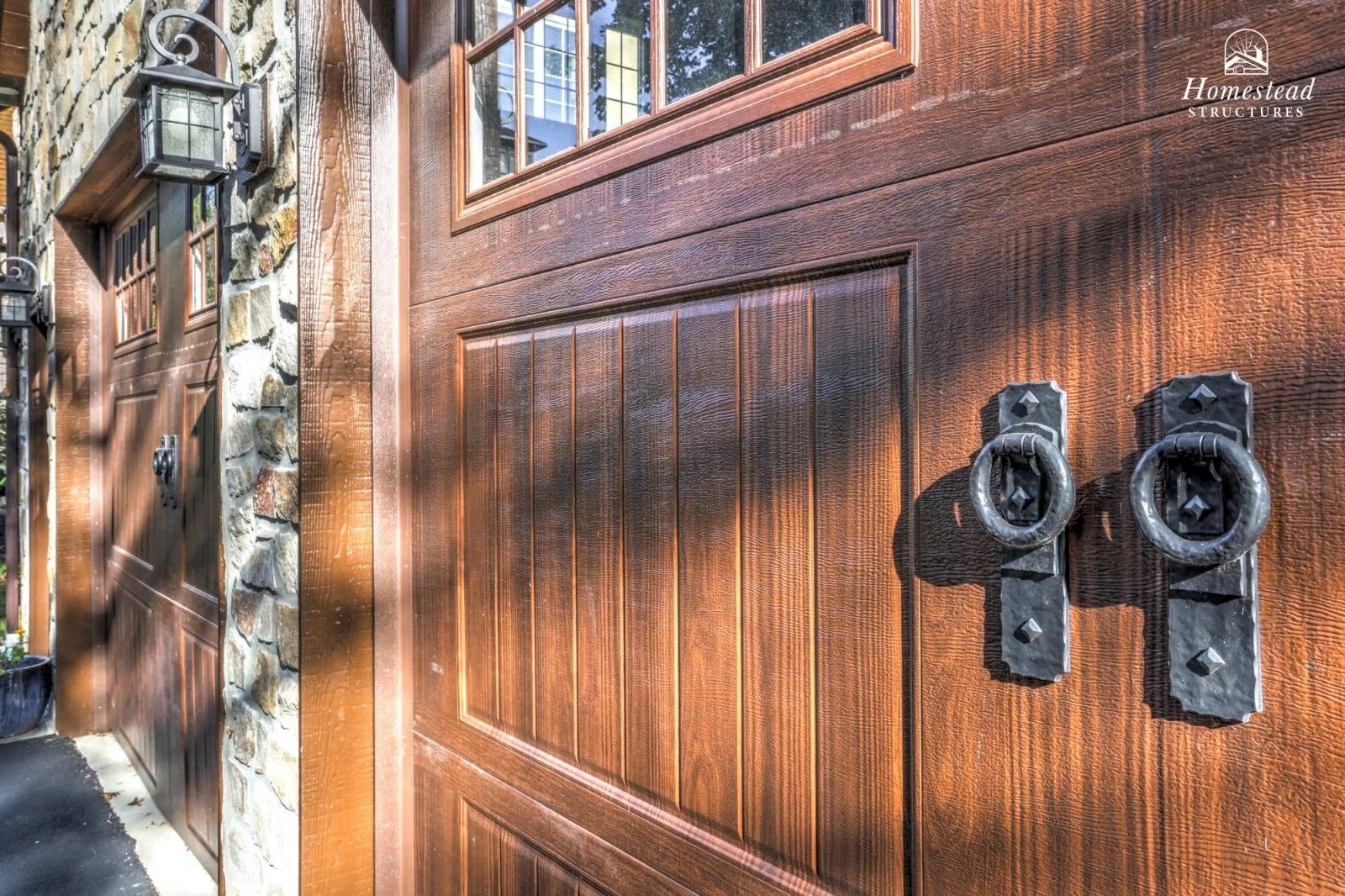 Close-up of a wooden garage door with black metal handles and stone and wood exterior wall.