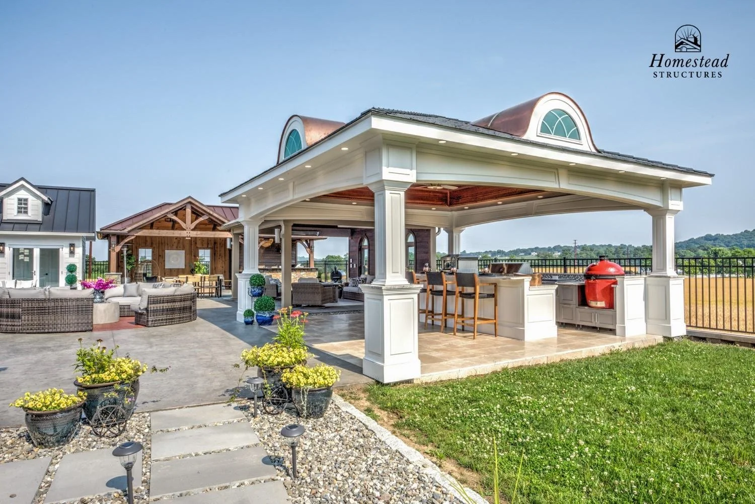 Outdoor rooftop patio with seating, a built-in bar, and a covered pavilion with a grill, set against a scenic landscape under a clear sky.