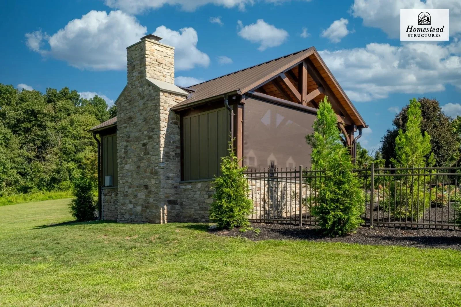 A small stone house with a chimney, surrounded by green grass and trees, under a partly cloudy sky.