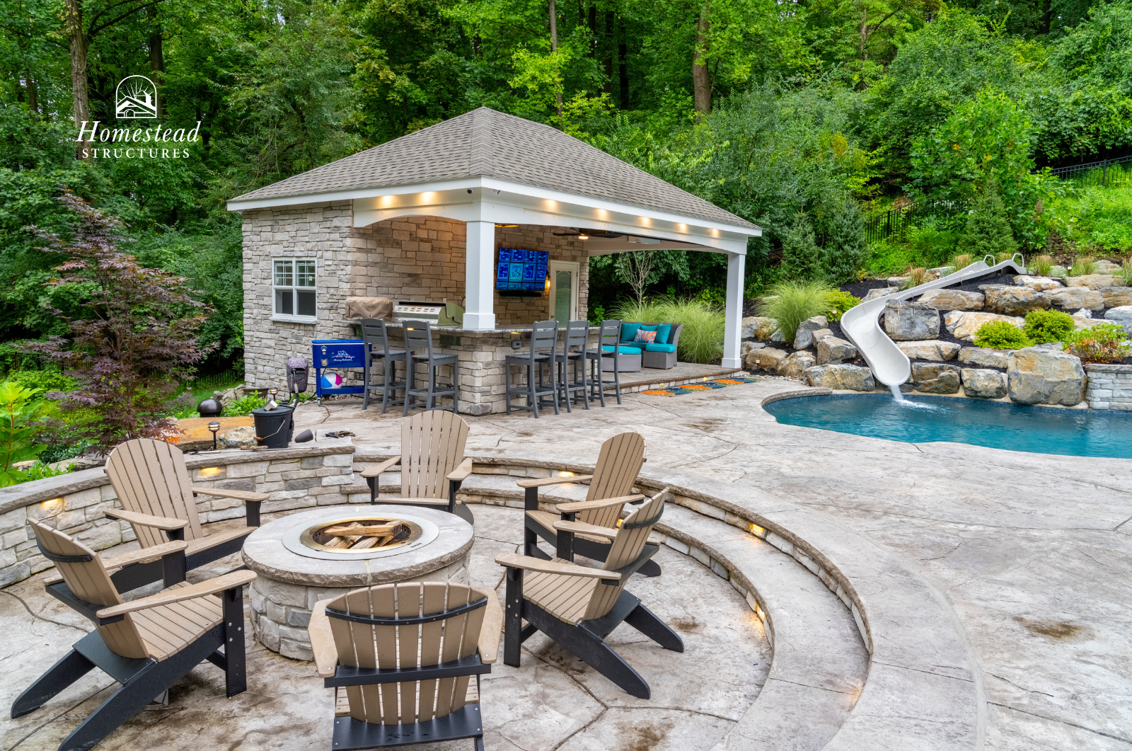 Outdoor backyard scene with a stone fire pit surrounded by Adirondack chairs, a pool with a waterslide, a covered bar area with stools, tree-covered hillside in the background, and landscaping.