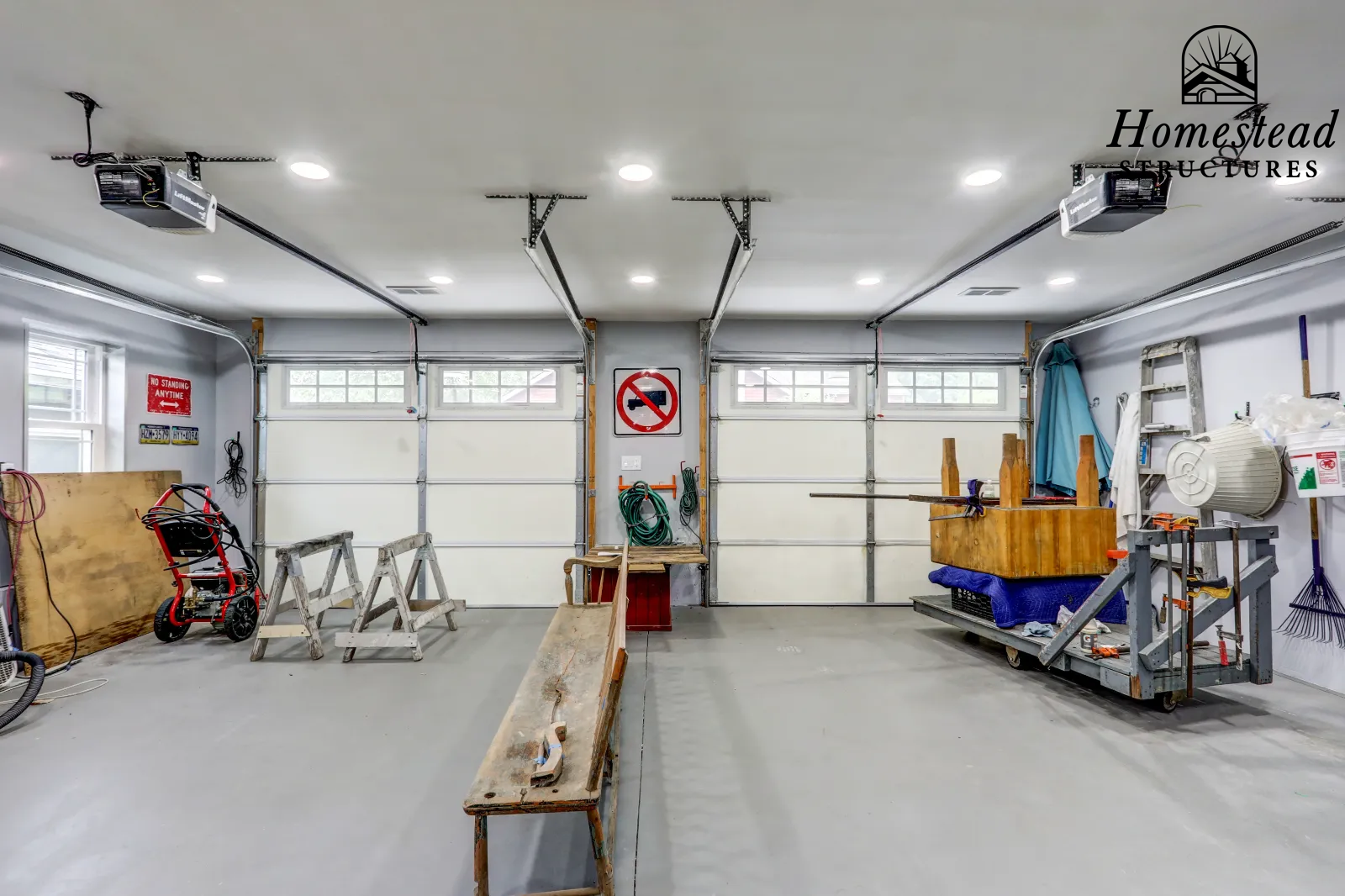 Empty garage with tools and equipment, including a workbench, ladder, and hoses, with bright overhead lighting.